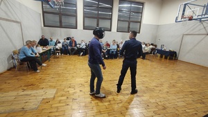 widzimy policjantów pokazujących chwyty obezwładniające oraz uczestników spotkania.