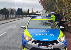 widzimy policyjny radiowóz stoicy na poboczu, a w tle policjantów.