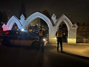 widzimy policjantów stojących przy cmentarzu obok widzimy policyjny radiowóz.