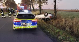 widzimy policyjny radiowóz oraz uszkodzony pojazd a także strażaków.