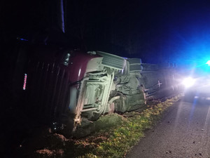 widzimy pojazd ciężarowy leżący na boku w rowie , a w tle widać światła błyskowe w kolorze niebieskim.