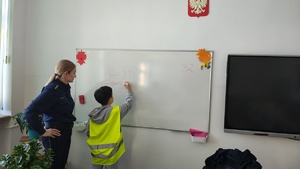 widzimy policjantkę z uczniem przy tablicy w klasie, który pisze.