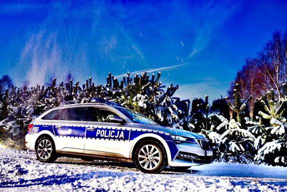 widzimy policyjny radiowóz w zimowej aurze na tle lasu.