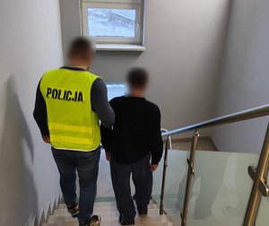 policjant prowadzi zatrzymanego klatką schodową.