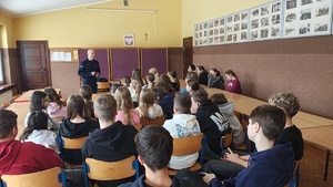 widzimy policjanta prowadzącego spotkanie z dziećmi siedzących w sali.