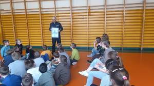 widzimy policjanta prowadzącego spotkanie z dziećmi siedzących w sali.