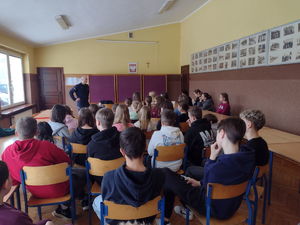 widzimy policjanta prowadzącego spotkanie z dziećmi siedzących w sali.