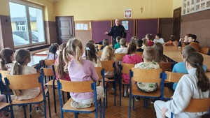 widzimy policjanta prowadzącego spotkanie z dziećmi siedzących w sali.