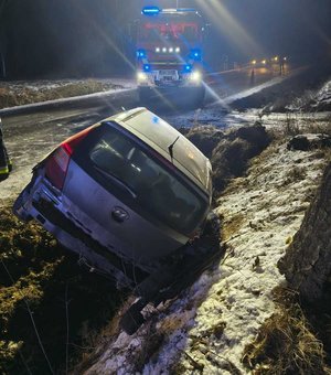 widzimy osobowy pojazd w rowie w miejscu zdarzenia, w oddali widać pojazd Straży Pożarnej.