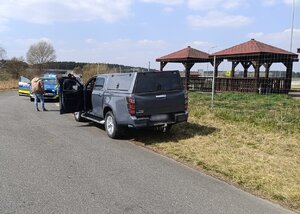 widzimy policyjny radiowóz oraz inny pojazd tupu pikap stojących na drodze wraz z funkcjonariuszami.