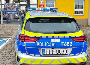 widzimy p[policyjny radiowóz na tle budynku oraz odznakę policyjna z napisem policja Wieruszów.