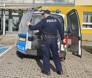 widzimy dzielnicowego przy radiowozie, w tle widać budynek komendy.