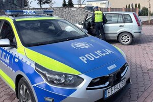 widzimy p[policyjny radiowóz oraz policjanta kontrolującego samochód.