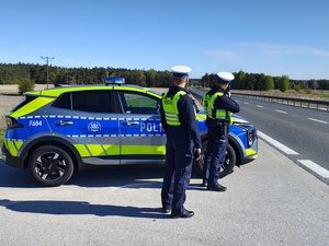 widzimy policjantów mierzących prędkość, stoją obok radiowozu.