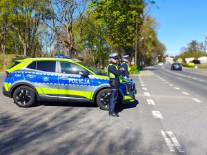 widzimy policjantów stojących przy radiowozie przy drodze.