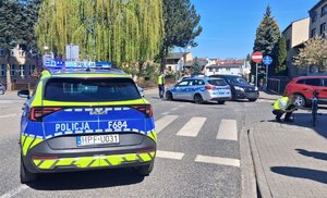 widzimy radiowozy stojące na jezdni oraz pracujących na miejscu policjantów.