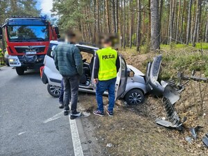 widzimy służby na miejscu wypadku w tym policjantów i uszkodzony samochód.