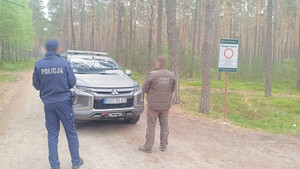 widzimy policjanta i funkcjonariusza Straży Leśnej w kompleksie leśnym na tle pojazdy straży leśnej.