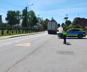 widzimy policjanta mierzącego prędkość na  tle policyjnego radiowozu.
