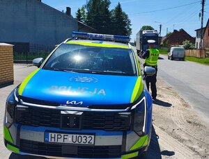 widzimy policjanta mierzącego prędkość na  tle policyjnego radiowozu.