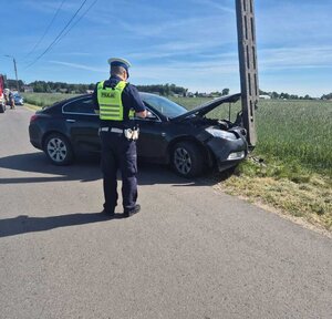 widzimy policjanta stojącego przy rozbitym samochodzie.