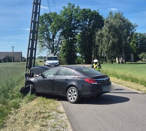 widzimy  rozbity samochód który wjechał w słup energetyczny, a w oddali policjanta i inny pojazd typu bus.
