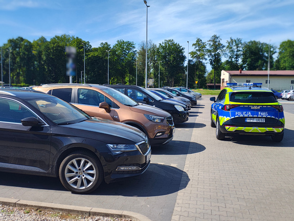 widzimy parking samochodowy oraz pojazdy i radiowóz policyjny.