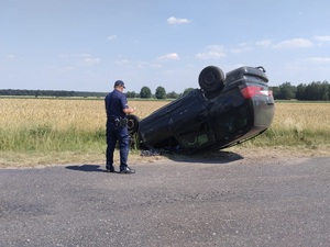 widzimy policjanta oraz wywrócony na dach samochód.