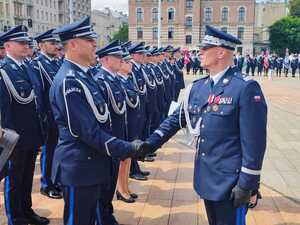 widzimy policjanta gratulującego innemu policjantowi oraz szereg policjantów stojących w rzędzie.