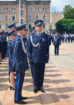 widzimy policjanta stojącego na baczność oraz szereg policjantów stojących w rzędzie.
