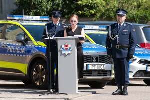 widzimy policjantów oraz kobietę stojącą przy mównicy, w tle widać policyjny radiowóz.