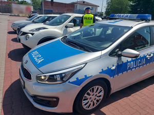 na zdjęciu widnieje policjant który sprawdza wnętrze pojazdu oraz radiowóz policyjny