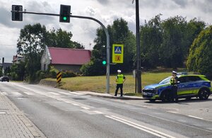 widzimy policjantów w rejonie przejścia dla pieszych wraz z oznakowanym radiowozem.