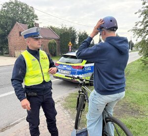 widzimy policjanta i rowerzystę zakładającego kas na głowę.