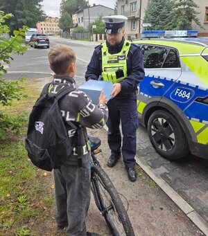 widzimy policjanta wręczającemu rowerzyście kask.