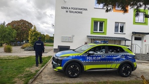 widzimy policyjny radiowóz na tle budynku szkoły oraz idącego policjanta.