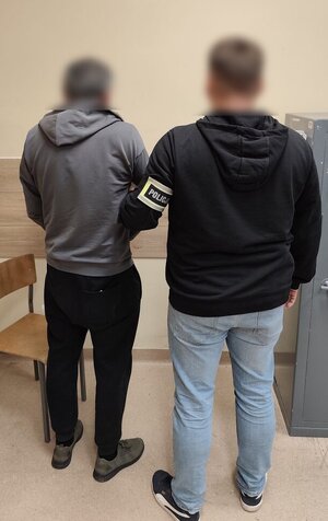widzimy zatrzymanego oraz policjanta trzymającego go za rękę.