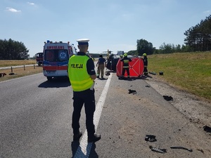 widać droge, na pierwszym planie policjanta, dalej straż pożarna  i parawan, na jezdni kawałki nadwozia pojazu